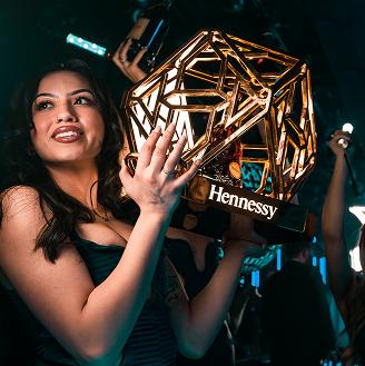 Person holding a geometric-shaped Hennessy object in a dimly lit environment.